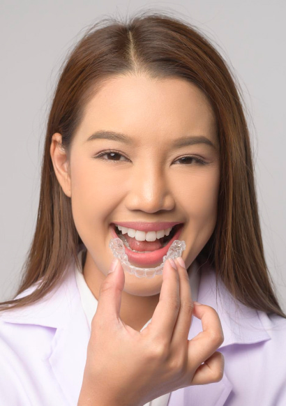 A girl smiling while taking in her hands a clear aligner